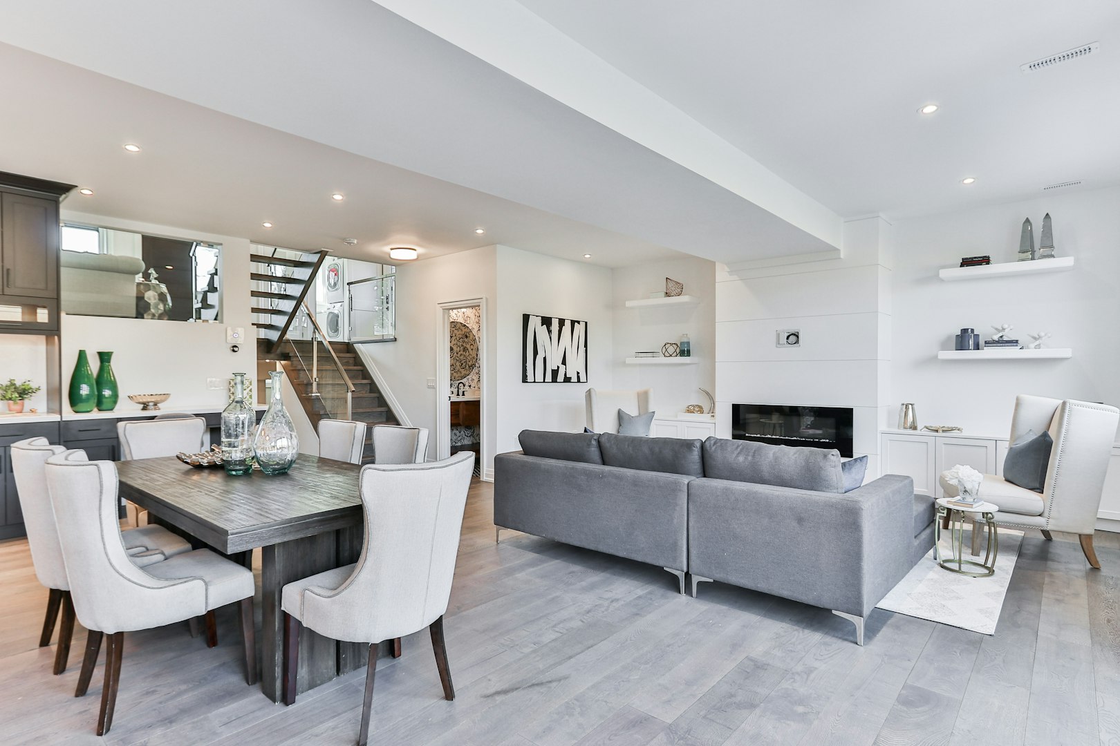 Modern dining room with a large table set for six, featuring gray walls and decorative accents, adjacent to a living area with a view of the backyard.